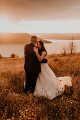 loving couple wedding newlyweds hug kissing in summer field on mountain above the river