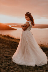 Fototapeta na wymiar bride in white wedding dress with a crown on her head stands on cliff against the background of the river and islands