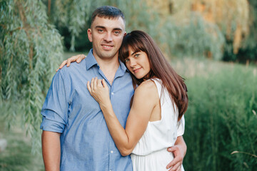 Beautiful married couple man woman in love. Husband and wife hugging in park on summer day at sunset. Togetherness and happiness. Authentic real people family outdoors.