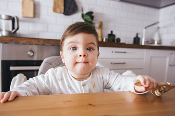 Boy baby sitting in high chair and laughing in a modern white kitchen. Healthy nutrition for kids. Cute toddler