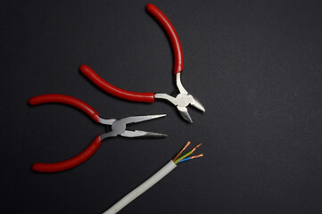 wire cutters, pliers and stripped wire lie against a dark background. close-up.