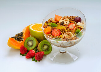 Glass bowl with yogurt with granola and fruits like strawberry, grape, banana, papaya, orange, kiwi on white background.