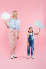 full length of cheerful mother and daughter holding thought bubbles on pink