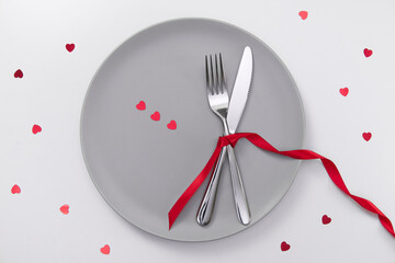 Valentine's day festive table setting, flat lay with red heart shape on gray plate, fork, knife and red ribbons on white table. Love dating concept. Place your text and copy space. High quality photo