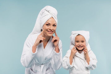 cheerful mother and kid in bathrobes smiling and touching cheeks isolated on blue