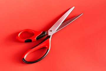 Opened steel red and black scissors on pink background. Professional cutting instruments.