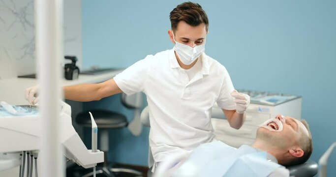 Dentist adjusting dental braces during orthodontic treatment for the young male patient. Doctor taking some dental tools from the table