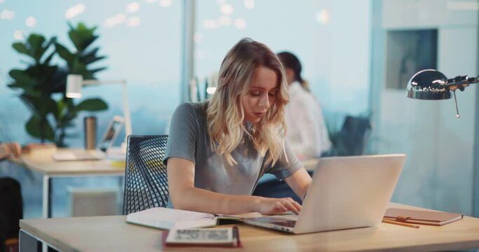 Blonde young executive woman using laptop at computer desk working inside shared corporate workspace. Business office. Businesswoman.