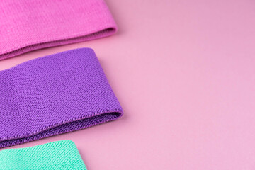 Colorful fitness gums on pink background. Elastic expanders and tapes of different color. Colored rubber and textile bands. Home fitness equipment.