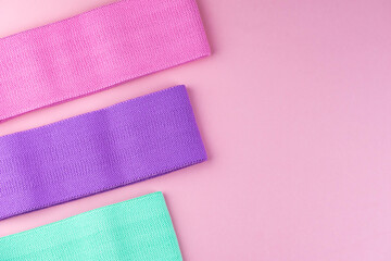 Colorful fitness gums on pink background. Elastic expanders and tapes of different color. Colored rubber and textile bands. Home fitness equipment.