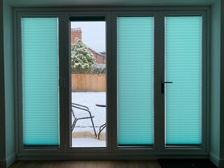 Funky green/blue blinds with a limited view to a snow-covered garden outside in Cheshire