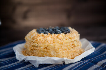 homemade napoleon cake decorated with crumbs and blueberries on a dark background