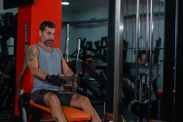 Fototapeta na wymiar Fitness training in sport gym of active male with beard sitting and pulling heavy weight on exercise equipment
