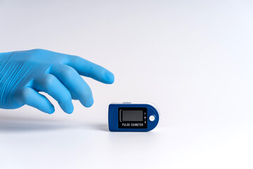 Pulse oximeter on a white background. A hand in a medical glove holds a device for health diagnostics