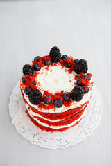 homemade red velvet cake decorated with berries on a light wooden background