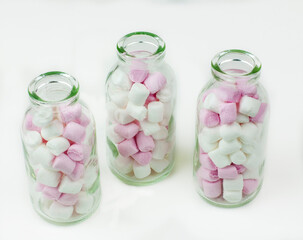 Sweet jelly beans in glass bottles on white background