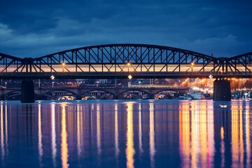 Fototapeta premium Passenger train passing over railway bridge against city. Cityscape of Prague at night, Czech Republic