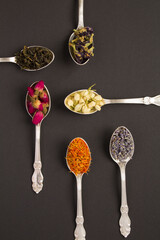 Top view of different varieties of tea in the silver spoons on the  black surface