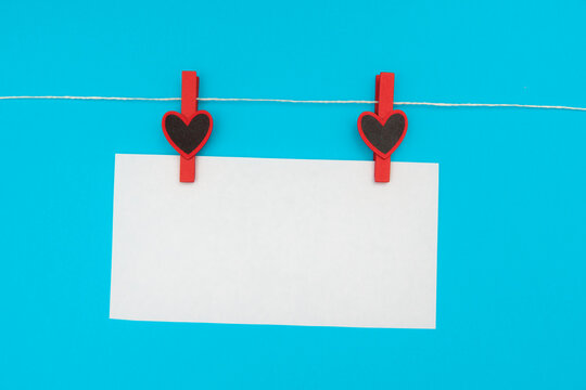 A clothespin with a heart holds a white sticker against the blue sky. Place for text you can write your greeting. Stretching on a rope. High quality photo