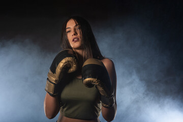 Closeup portrait of a female boxer posing with boxing gloves and looking at the camera with a smokey background