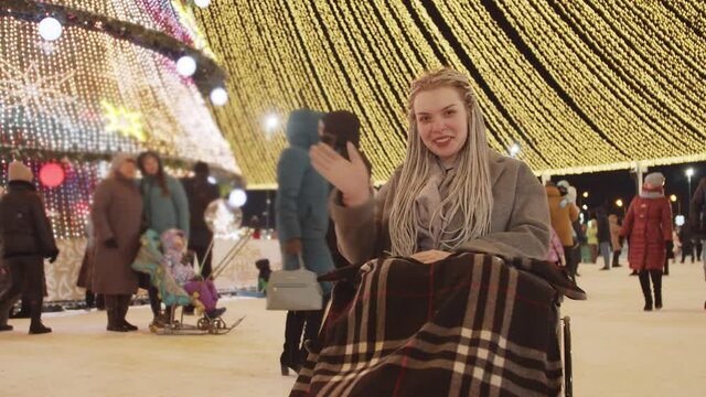 Young positive woman in a wheelchair at Christmas celebrating on the streets - smiling and waving her hand