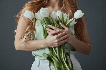 Woman with long wavy blond hair holding a bouquet of white tulips in her hands