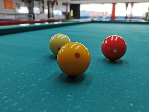 Bolas de billar a tres bandas, bolas roja, blanca y amarilla, sobre mesa de billar de pa&ntilde;o verde