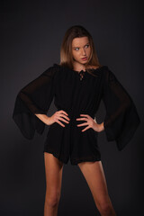 Pretty brunette girl with little black dress posing isolated on dark background in studio