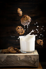 Chocolate Chip Cookie with a splash of milk in glass. Wooden rustic table, black background. Healthy oatmeal biscuits with milk drops, food levitation art photo concept. Copy space.
