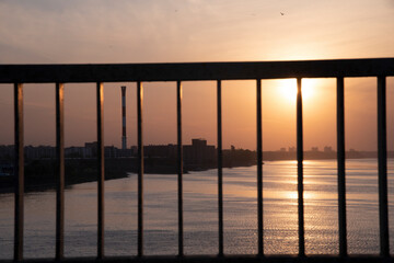 View of the Danube river and the city of Belgrade trough the metal fence of Pancevo Bridge (Pančevački most) at sunset. Orange sky and clouds in background.