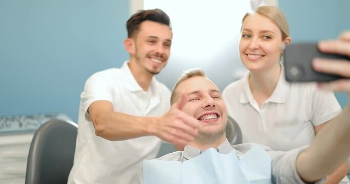 Young male patient in dental braces making selfie photo with a dentist and assistant during a regular orthodontic visit at the dental office. Happy dental appointament concpet