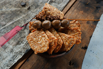Quail egg satay and fried tempeh on wooden table. Yogyakarta typical angkringan food menu
