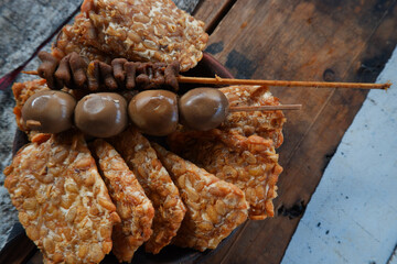 Quail egg satay and fried tempeh on wooden table. Yogyakarta typical angkringan food menu