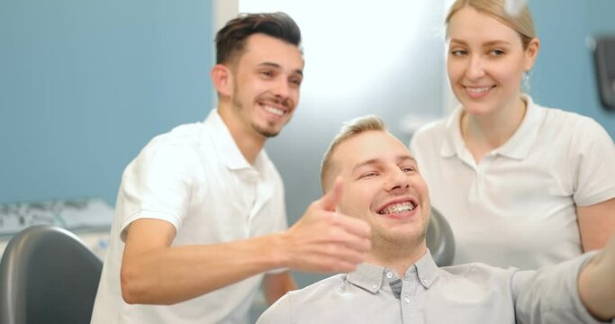 Young male patient in dental braces making selfie photo with a dentist and assistant during a regular orthodontic visit at the dental office. Happy dental appointament concpet