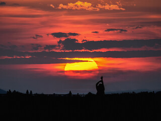 Fototapeta na wymiar Silueta a contraluz de una mujer con los brazos levantados al atardecer con el sol en grande y las nubes