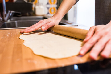Hands using a rolling pin to shape the dough on the kitchen counter