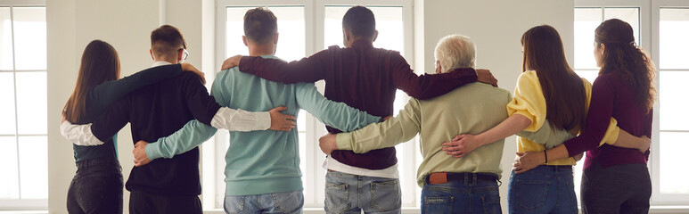 Team of people hug standing in a row with their backs to the camera and looking out the window....