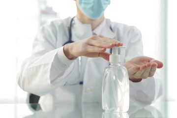 Doctor with a stethoscope in a protective mask in a clinic treats his hands with an antiseptic. Close-up