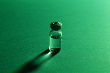 Vial with vaccine on green background