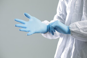 Doctor in a protective suit puts on blue rubber gloves