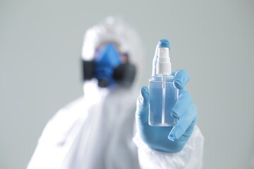 Doctor in a protective suit in a respirator of protective glasses holds an antiseptic spray in his hand