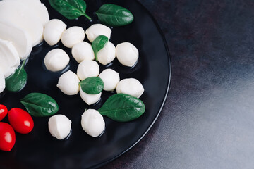Obraz na płótnie Canvas White small mozzarella cheese balls, spinach leaves and tomatoes on black plate.