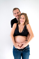 Fototapeta premium Portrait of young pregnant couple smiling happy putting their hands together in a heart shape on top of their belly