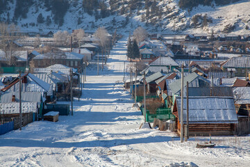A village in the winter, located among the mountains. Houses, sheds, haystacks.