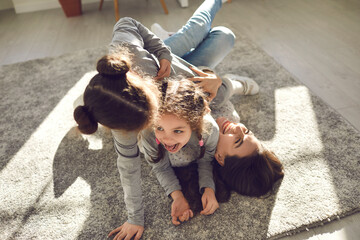 Happy family enjoying quality time at home. Mom and little children frolicking on carpet. Cheerful...