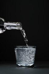 Mineral water is poured into a glass, close-up, dark background with copy space, selective focus.