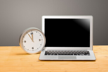 mocap Laptop and clock with arrows at five to twelve on a wooden table.