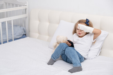 Little girl with hand in cast sitting in bed using smartphone