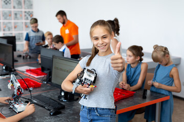 Portrait of a happy schoolgirl girl in a robotics class, she holds a robot assembled from plastic parts programmed on a computer