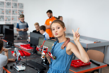 Fototapeta na wymiar Portrait of a happy schoolgirl girl in a robotics class, she holds a robot assembled from plastic parts programmed on a computer